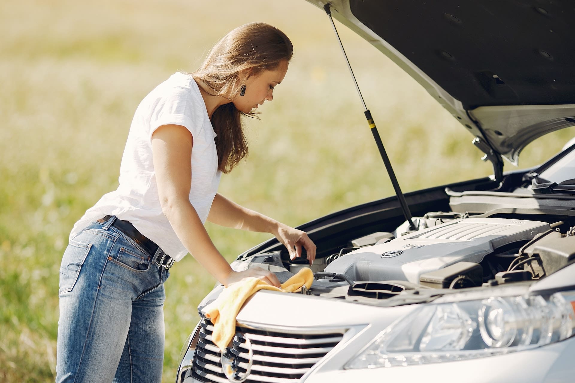 young woman looking at the hood of her broken down car on a road